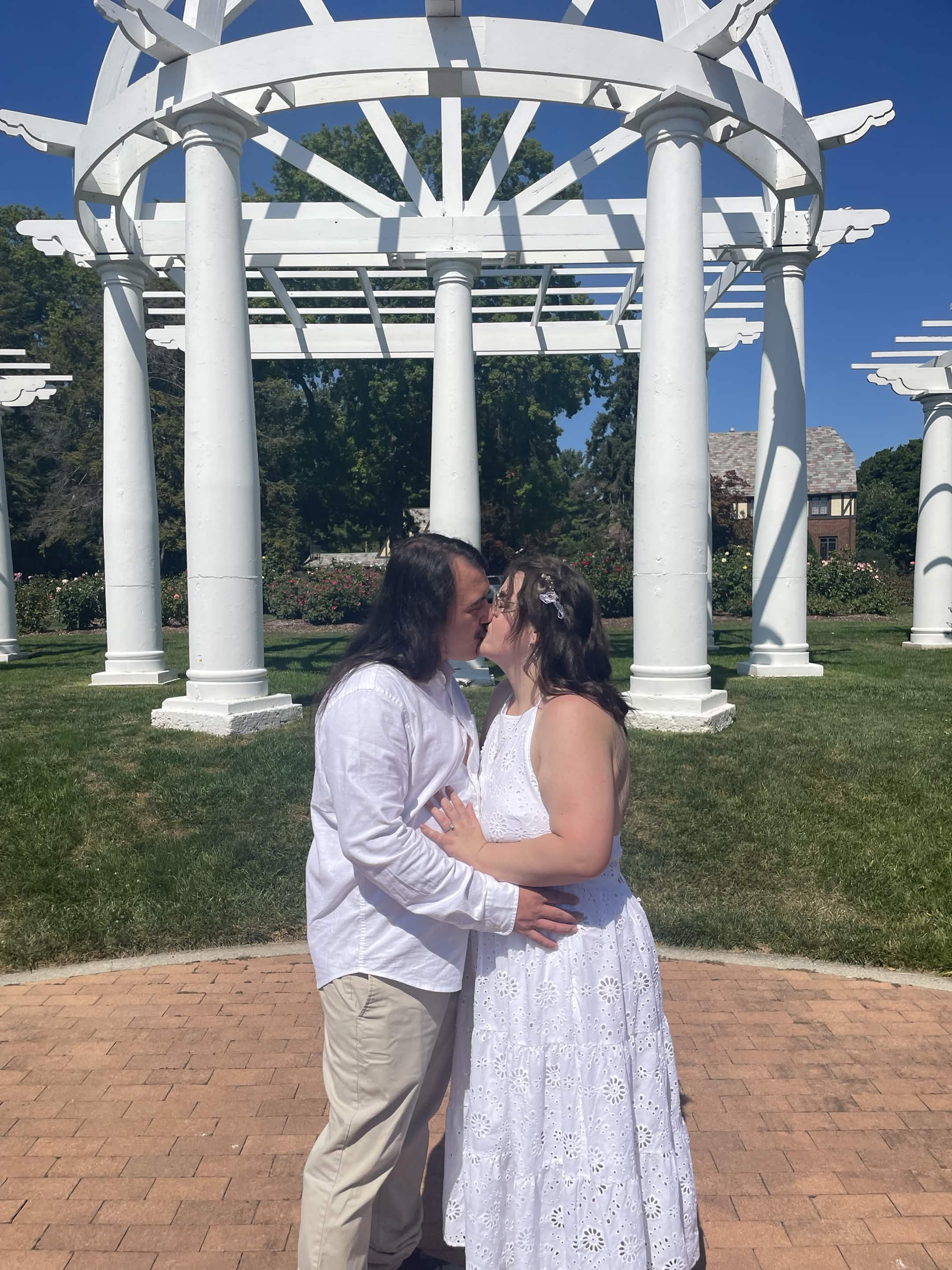 Newlyweds kissing under a white pergola in a rose garden